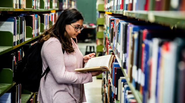 A female student reads a book while in the stacks at Weldon Library